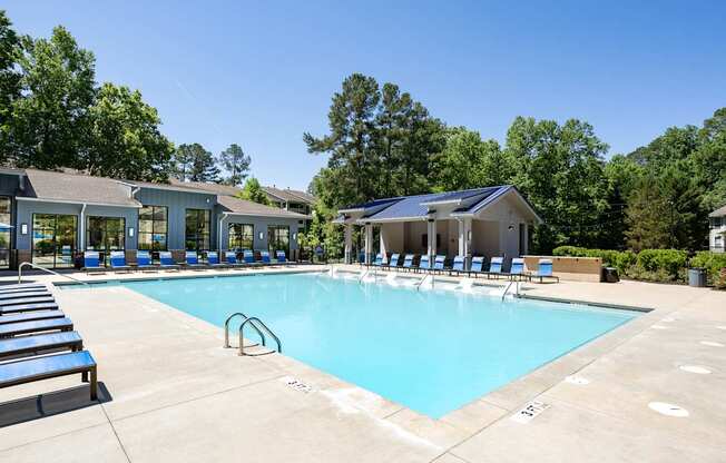 A large swimming pool with sun loungers and a building in the background.