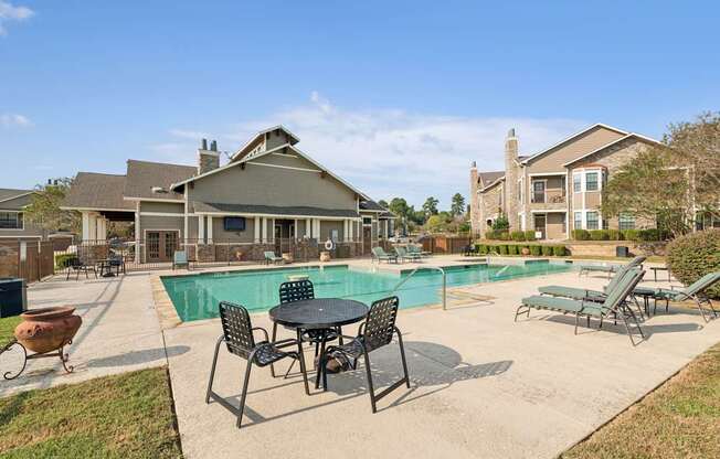 A pool area with a table and chairs in front of a building.