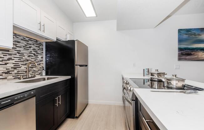 Apartments in Phoenix, AZ - Monaco31 - Renovated kitchen with quartz countertops, stainless steel appliances, white cabinets, all-electric kitchen, breakfast bar, and wood plank flooring