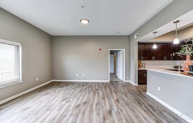 A room with wooden flooring and a kitchen area in the background.