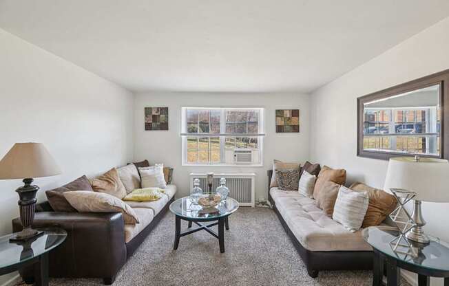A living room with a brown couch, a glass table, and a window with a view of the city.