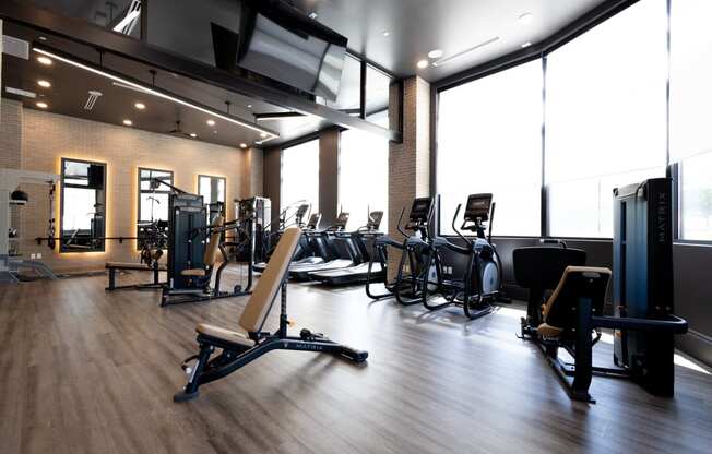 a large fitness room with cardio equipment and windows