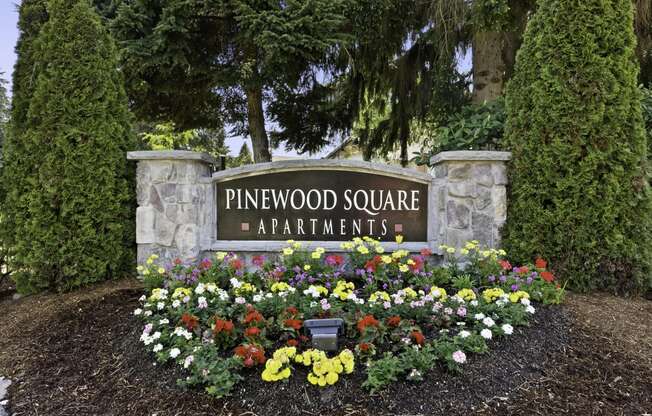 Stone Welcome Sign to Pinewood Square Apartment Homes with Flower Bed Below at Pinewood Square Apartment Homes, WA 98087