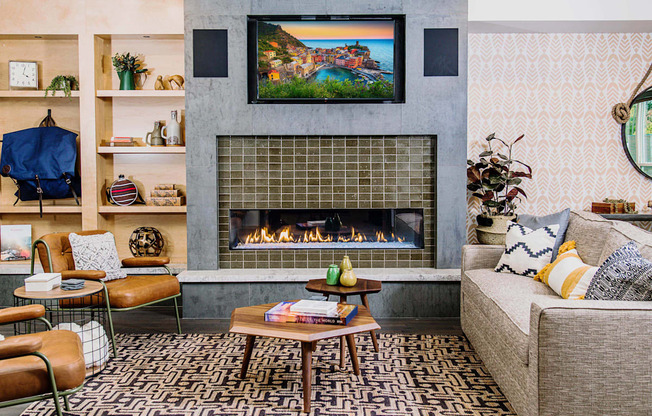 Cozy communal lounge in the apartment complex featuring stylish seating arrangements, a modern flat-screen TV, a warm fireplace, and a tabletop shuffleboard for residents to enjoy.