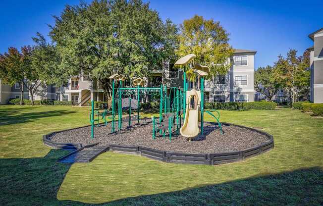 A playground surrounded by grassy lawns and mature trees at Saxony at Chase Oaks Apartments in Dallas, TX, offering a family-friendly recreational space.
