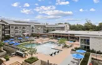 A large outdoor swimming pool with loungers and umbrellas is surrounded by apartment buildings.