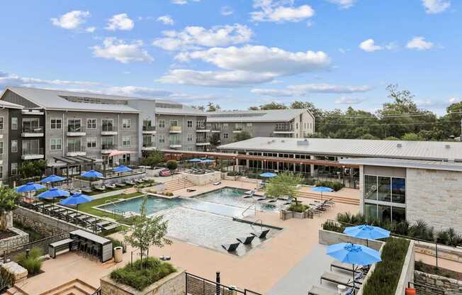A large outdoor swimming pool with loungers and umbrellas is surrounded by apartment buildings.