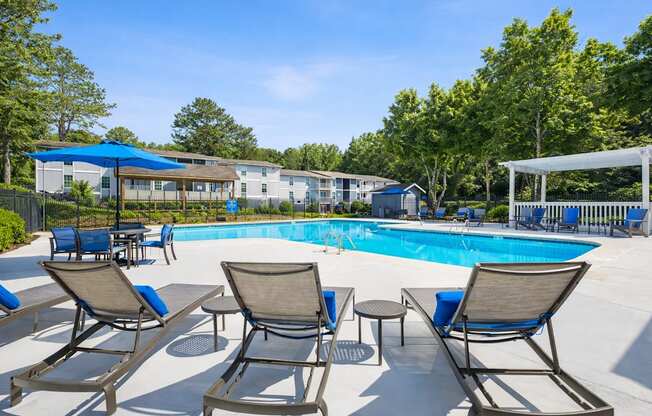 A pool surrounded by chairs and trees.