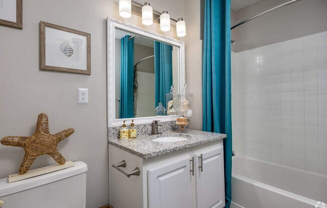 A bathroom with a white toilet, a sink with a mirror above it, and a blue shower curtain.