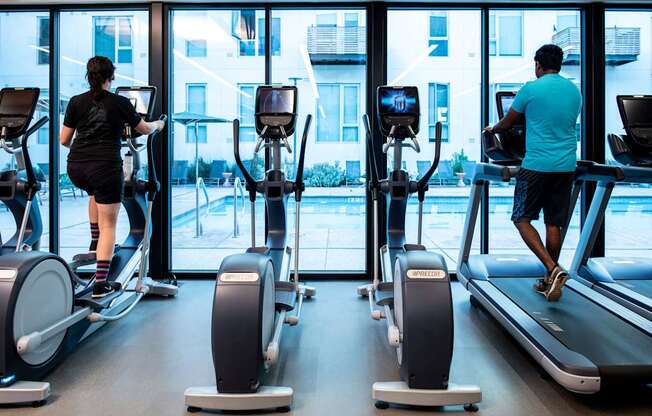 A man and a woman are exercising on treadmills in a gym.