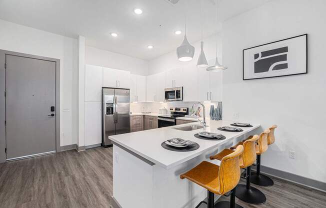 A modern kitchen with a long white island and wooden chairs.