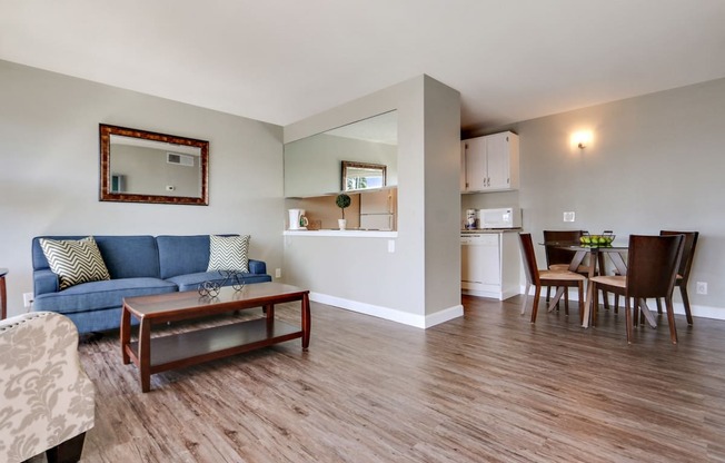 Living room with open kitchen on the left and dining area, wood style floors throughout, brightly lit