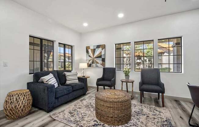 A living room with a dark blue couch, two chairs, and a woven ottoman.