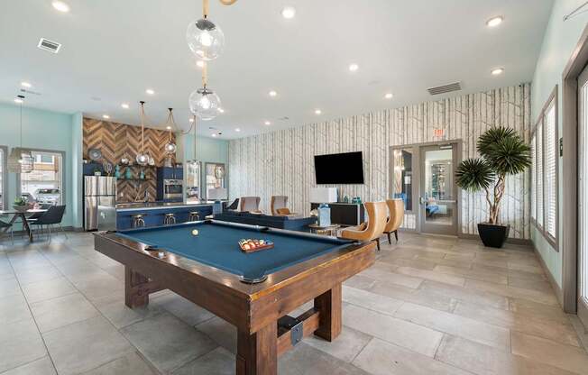 A pool table is in the middle of a room with a tv and a plant.