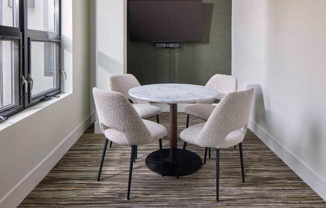 A white round table with four chairs in front of a grey wall and a television.