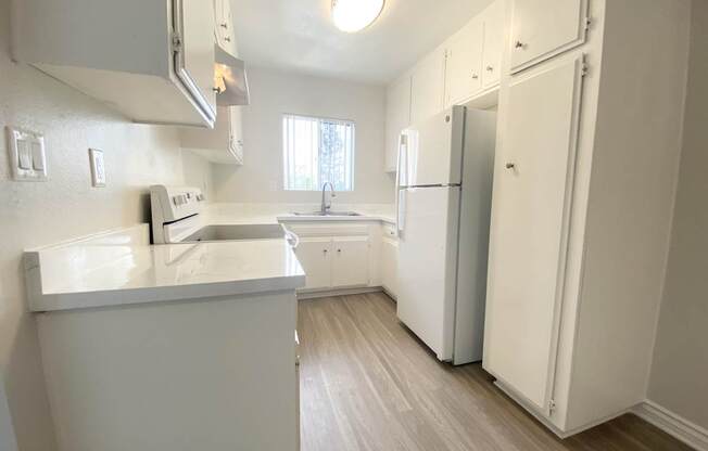 an empty kitchen with white cabinets and a white refrigerator