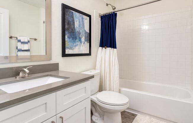 Bathroom with a white vanity, gray countertop and tiled tub with a navy and white shower curtain at Icon Avondale Apartments in Decatur, GA.