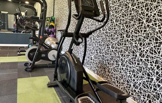 A treadmill with a monitor on top is in a gym with a patterned wall.