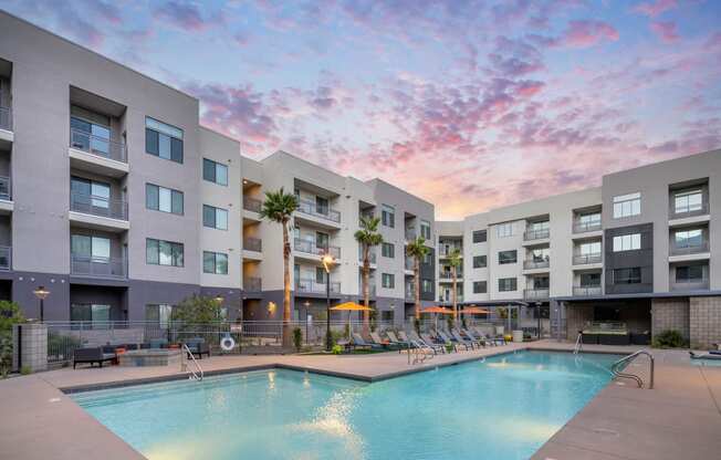 a swimming pool at an apartment complex with a sunset in the sky