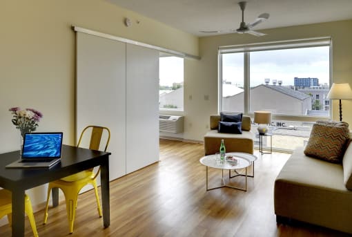 Table with yellow chairs and living area with couch in the Flat H, 1 bedroom floor plan at Coze Flats