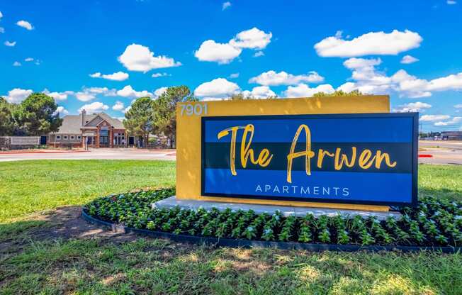 a blue and yellow sign for the apartments on a lawn with a street