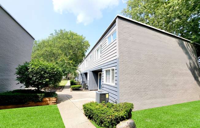 the exterior of a gray building with a sidewalk and grass