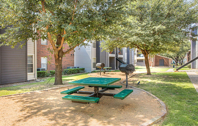 A green picnic table is in the middle of a sandy play area.