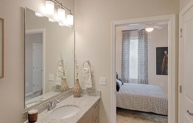 A bathroom with a sink, mirror, and a bedroom in the background.