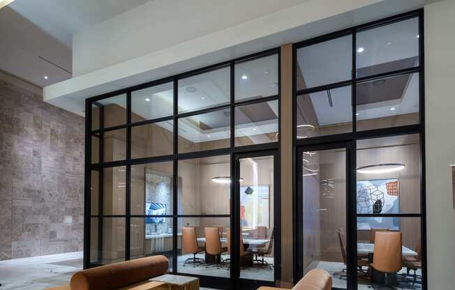 Lobby space with two modern couches next to a wall of windows looking into two conference rooms, one with 6 chairs and one with 4. There is an HDTV visible on the wall of the larger conference room.