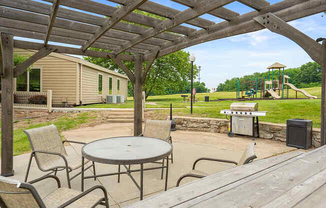 a patio with a table and chairs and a playground in the background