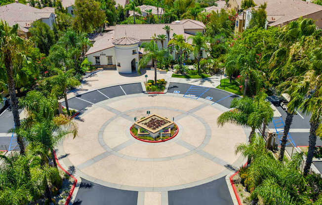 A courtyard with a fountain surrounded by palm trees and houses.