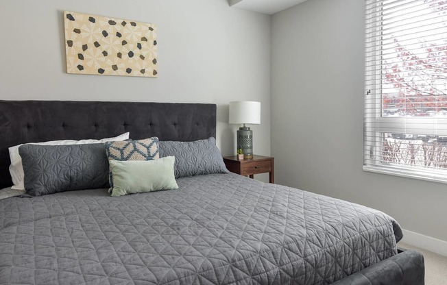 A bed with a black headboard and grey comforter with four pillows on it.