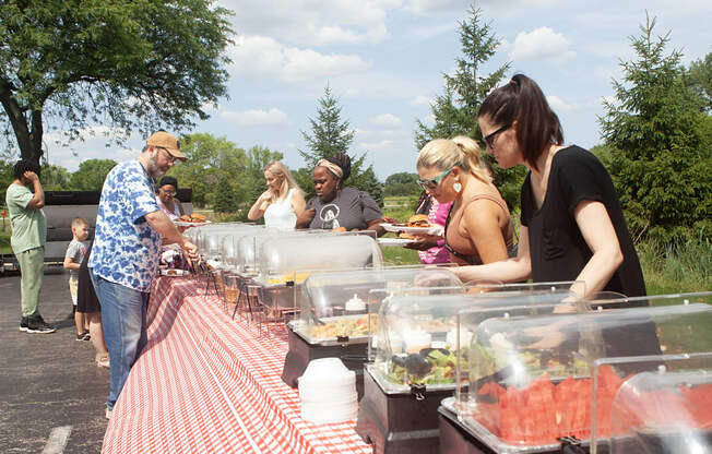 people lined up at an outdoor buffet table with a red and white checkered table cloth