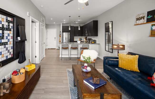 a living room with a blue couch and coffee table and a kitchen in the background  at Abberly Noda Vista Apartment Homes, North Carolina