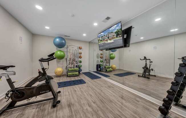 A home gym with a variety of exercise equipment including a stationary bike, a treadmill, and a television mounted on the wall.