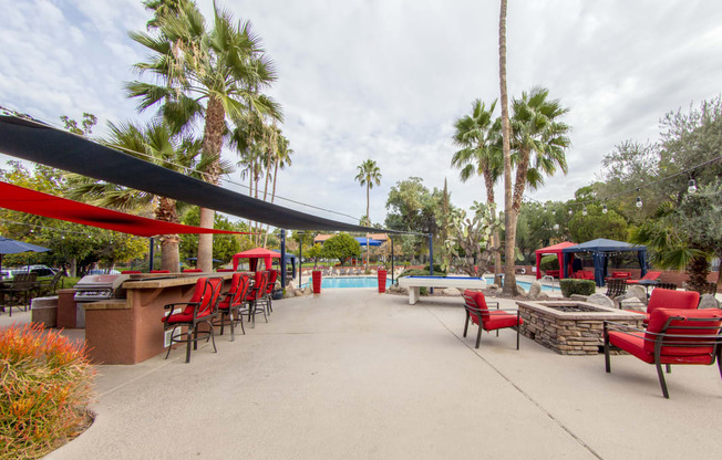 a patio with red chairs and tables and a pool with palm trees