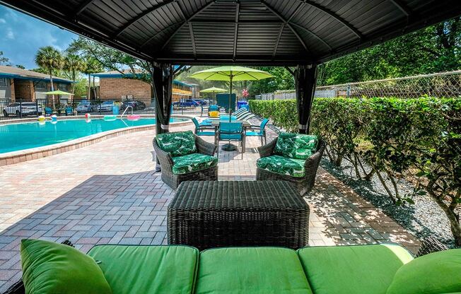 Poolside lounge at the Watermark Apartments in Lakeland, Fl with cushioned wicker patio seating and table under large shade.