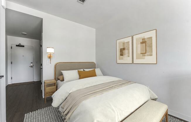 A bedroom with a bed, nightstand, and two framed pictures on the wall.