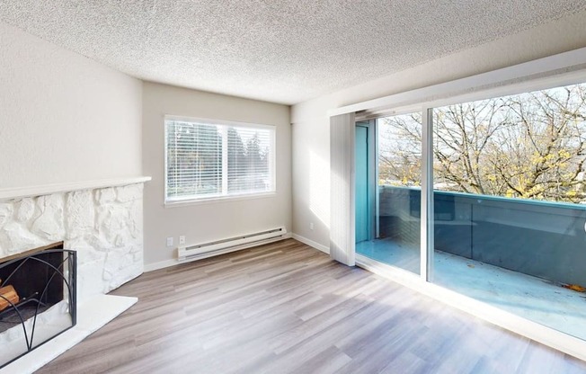 Sun-filled living area at Peak 88 Apartments Renton WA showcasing a fireplace, wood-style floors, and balcony views of trees.