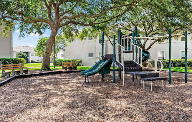 A playground with a green slide and a tree.