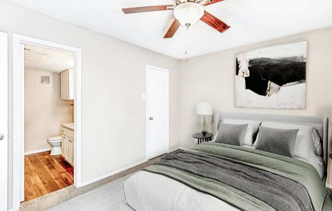 Virtually staged bedroom with carpet, accent rug, bed, nightstand with lamp, ceiling fan with light, en-suite bathroom and closet door