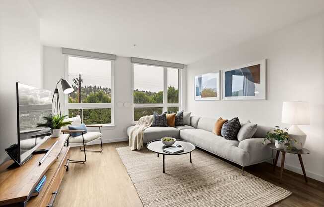 A modern living room with a grey sofa, a coffee table, and a large window overlooking a green landscape.