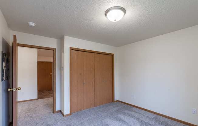 an empty living room with carpet and a door to a closet. Fargo, ND Oxford Apartments