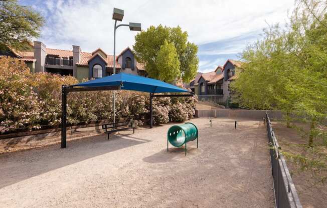 a playground with a blue tent and a green chair and houses