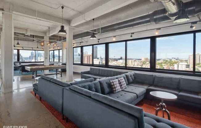 A large grey couch with pillows is in the center of a room with a view of the city at Archer Tower in Denver, CO