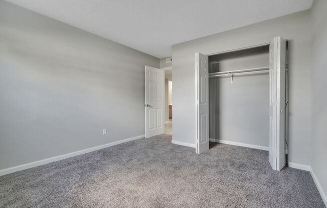 A room with a grey carpet and white walls with a doorway leading to another room.