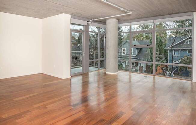A room with wooden floors and a balcony with a view of houses.