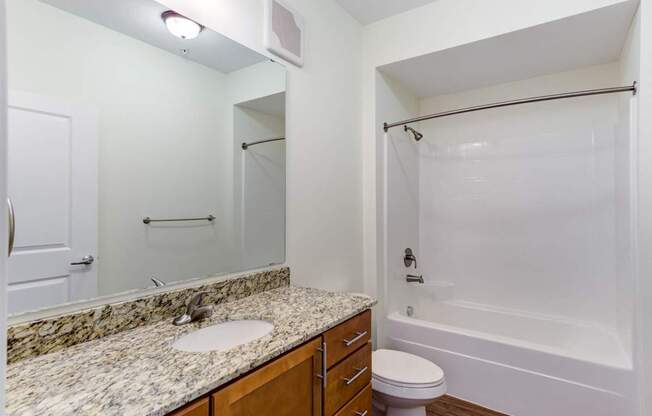 A bathroom with a marble countertop and a white tub.