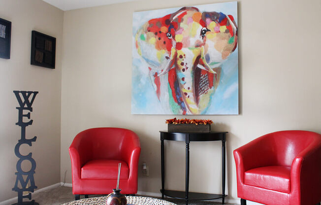 a living room with a large painting of an elephant on the wall and two red chairs