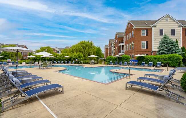 a swimming pool with chaise lounge chairs and umbrellas in front of a brick building